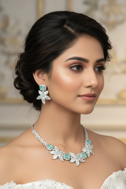 A set of American diamond jewelry including a necklace and earrings, predominantly silver in color with intricate designs and sparkling stones displayed against a white furry background.