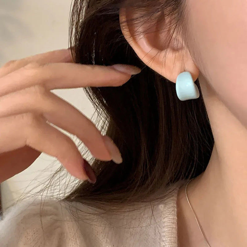 Close-up of a person wearing a light blue earring with a neutral background