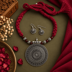 Black oxidized round pendant necklace with intricate silver-tone detailing, red braided thread and matching oxidized earrings