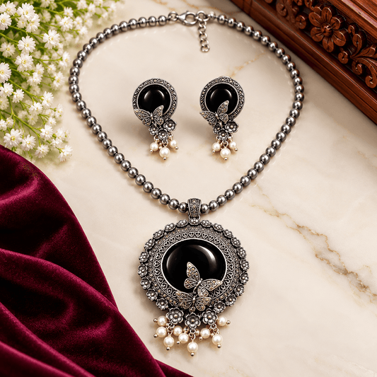 Black stone butterfly pendant necklace with oxidized silver-tone floral detailing, beaded chain, pearl-like drops, and matching earrings