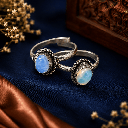 Pair of blue opal-style toe rings with oval stones and oxidized silver-tone decorative settings by The Mirage Fashion.